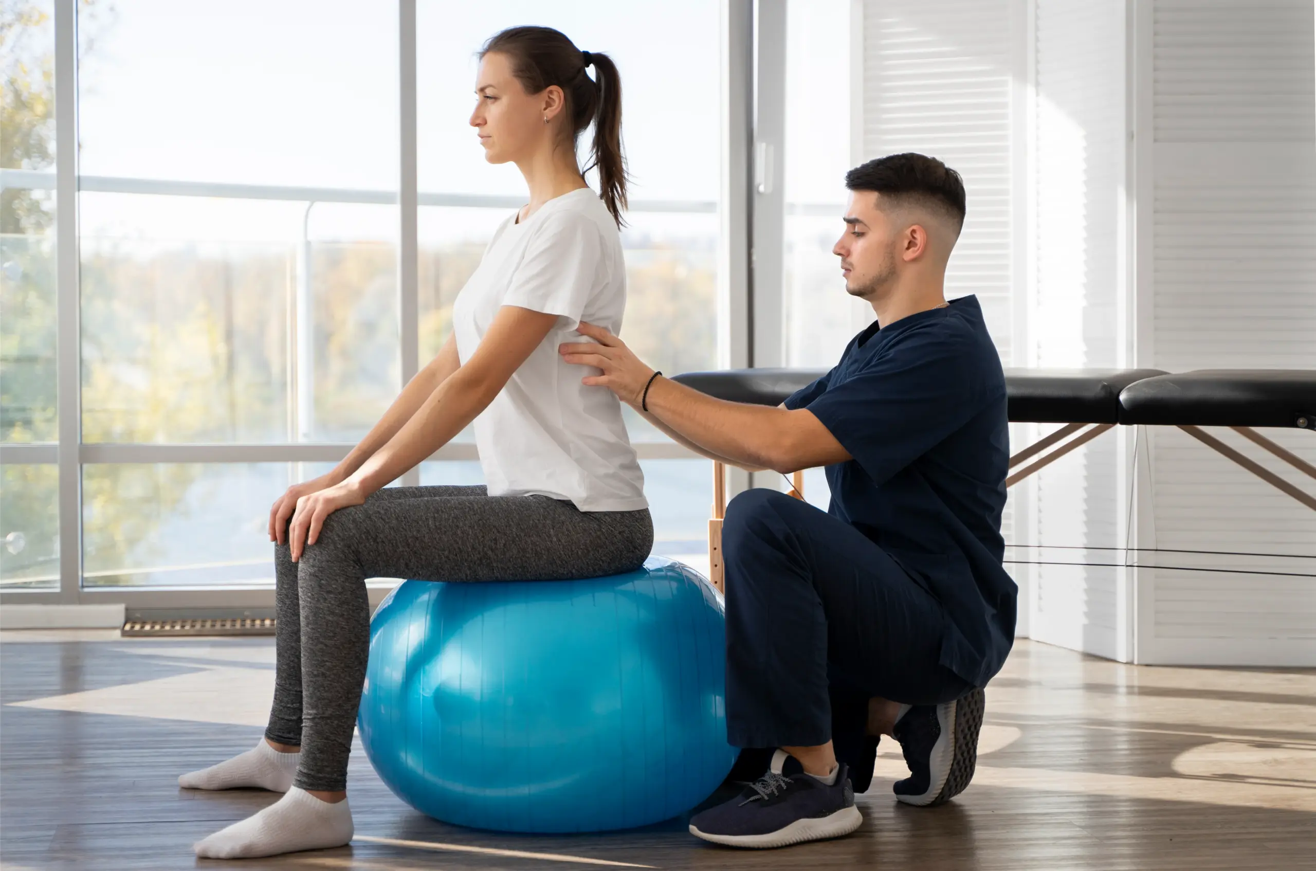 Physical therapist assisting a patient on a stability ball in a bright therapy room, emphasizing hands-on care and rehabilitation at Bal Therapy, LLC.